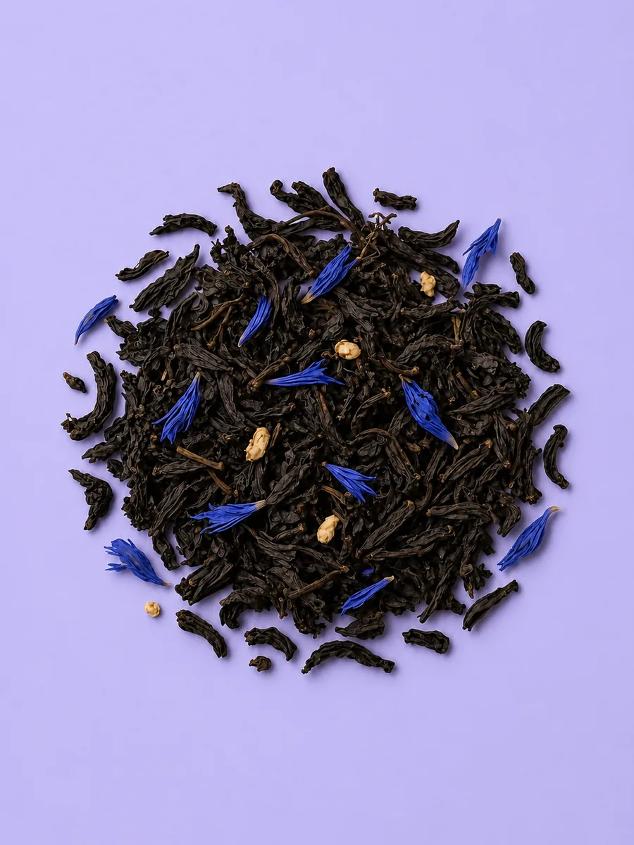 Hojas de té negro con flores de aciano sobre fondo lavanda